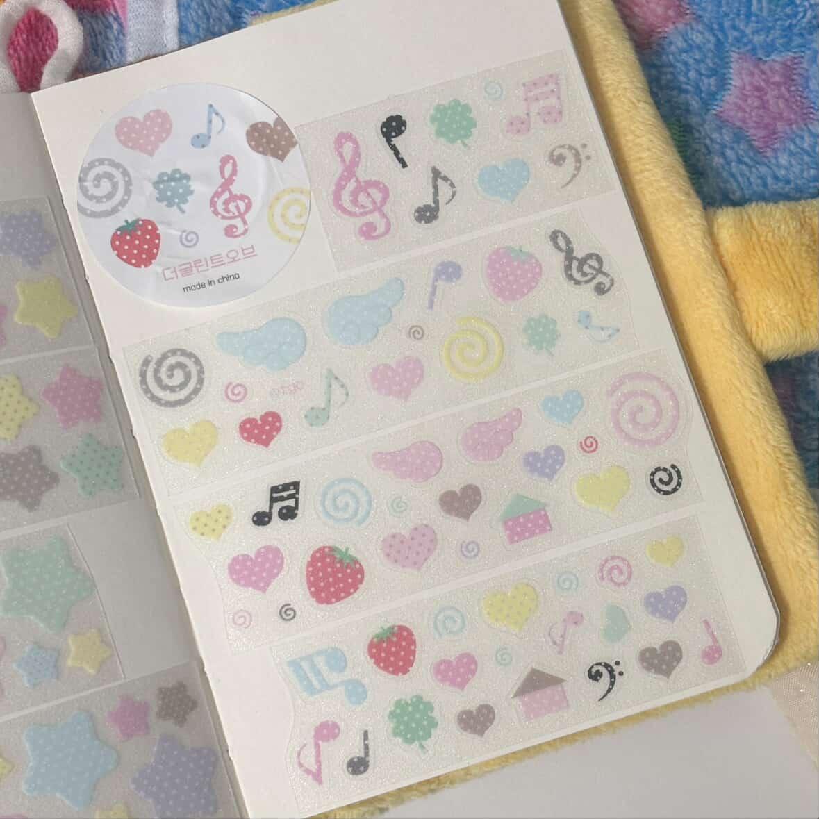 Sheet of colorful stickers with musical notes, hearts, and other designs on a textured surface.
